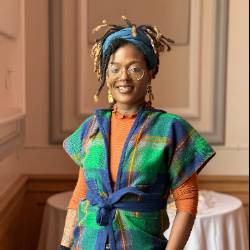 a headshot of an artist with dreads wearing a colorful vest