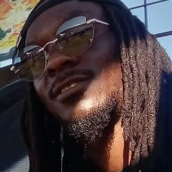 A headshot of an artist with dreads and sunglasses