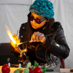 A headshot of an artist wearing a beanie and blowing glass