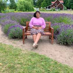 An artist sits at a park bench wearing a pink sweater