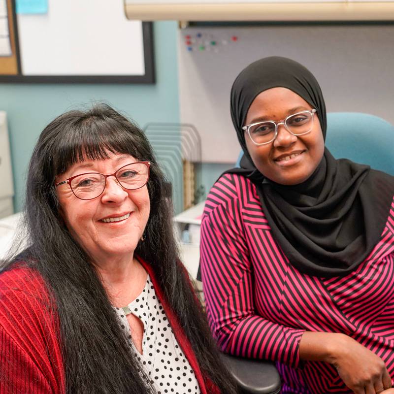 An accounting student and professor sit at a desk smiling