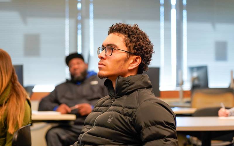 A student wearing a black jacket sits attentively in class