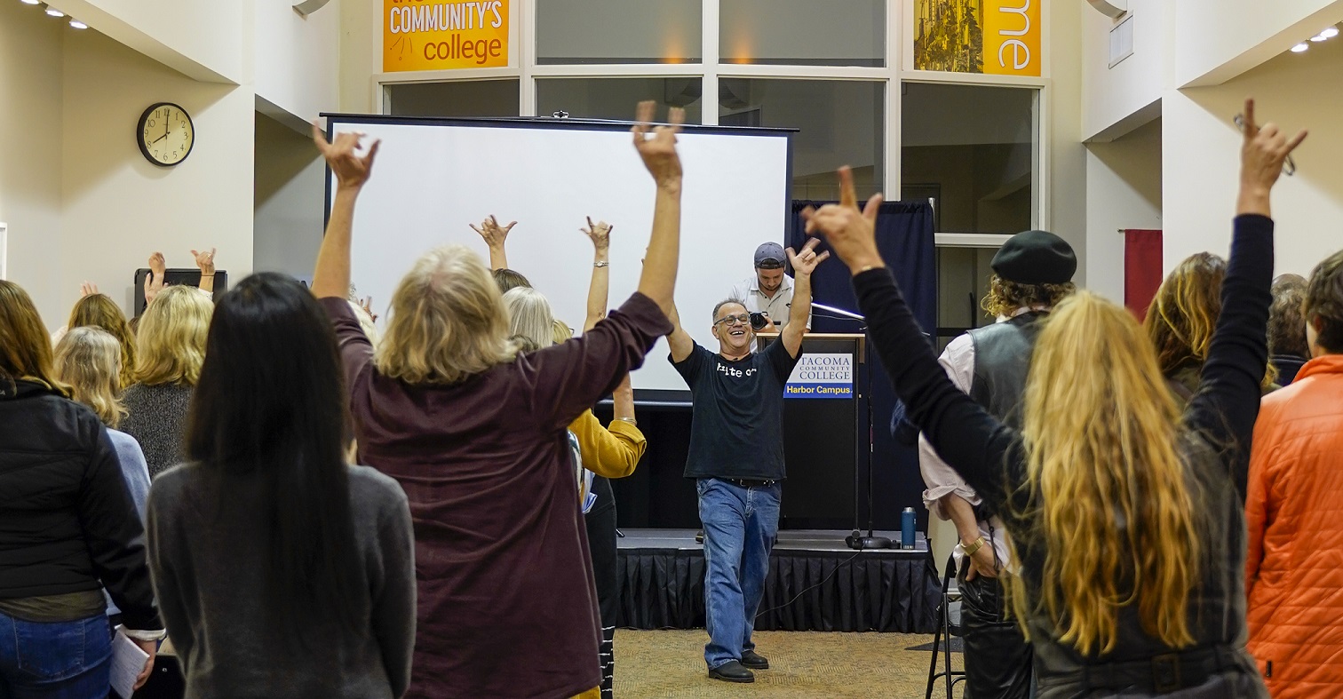 Keynote speaker Jeff Leisawitz is all smiles in front of conference attendees, many hands in the air with the "I love you" hand gesture.