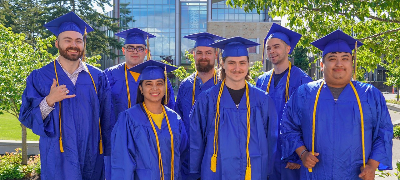 A group of graduates in blue caps and gowns pose in the campus commons