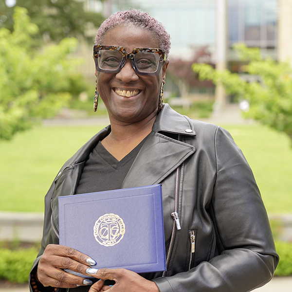 grad wearing a black leather jacket holding a diploma