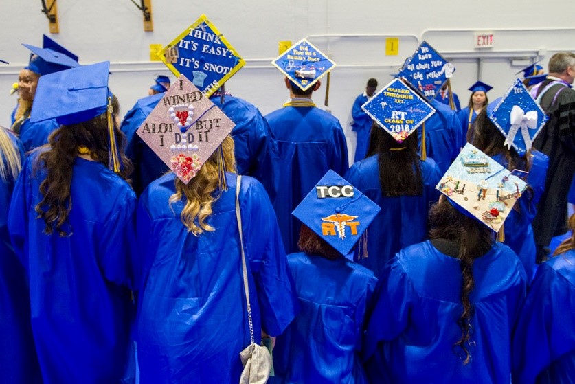 students in commencement regalia pose with the backs to camera, revealing a variety of messages on their hats