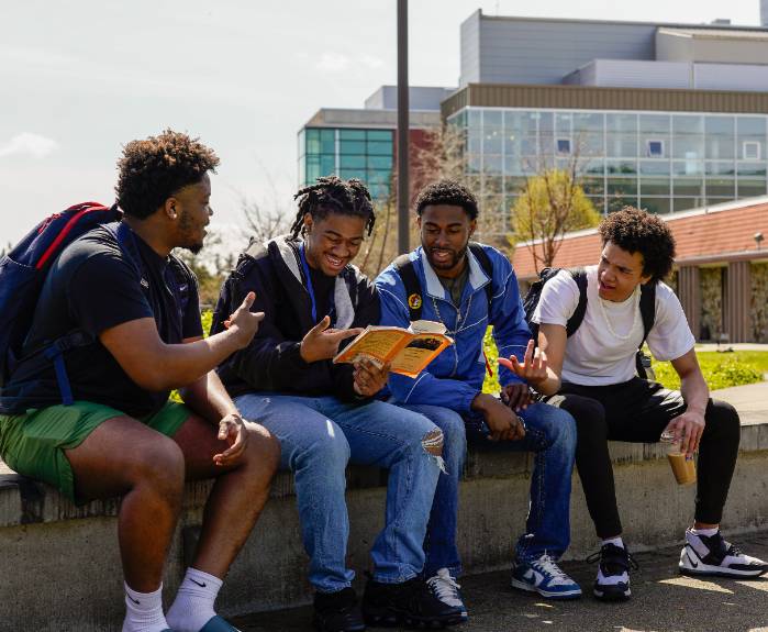 Four students sit in the campus commons and look at a book